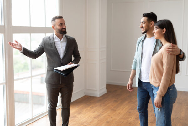 Immobilienmakler präsentiert eine Wohnung einem jungen Paar in einem hellen Raum.