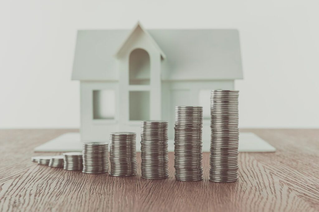 Münzstapel vor Holzhaus – Eigenkapital für Immobilienkauf