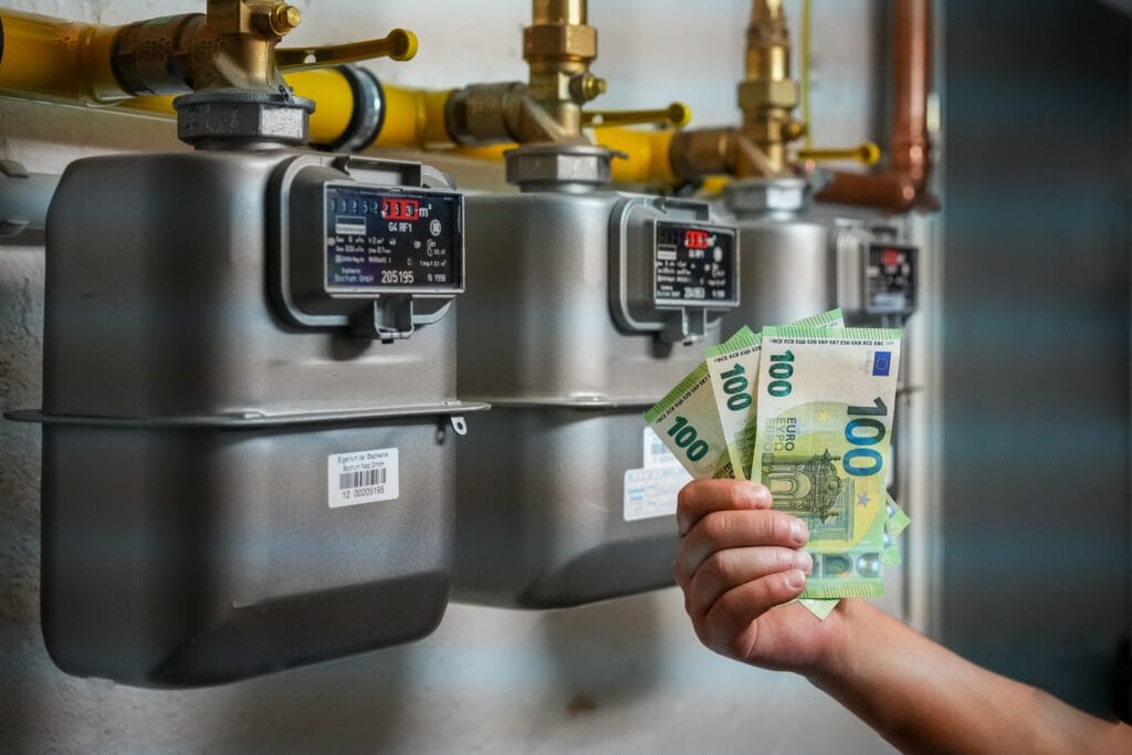 Eine Person hält mehrere Hundert-Euro-Banknoten in der Hand vor Gaszählern.